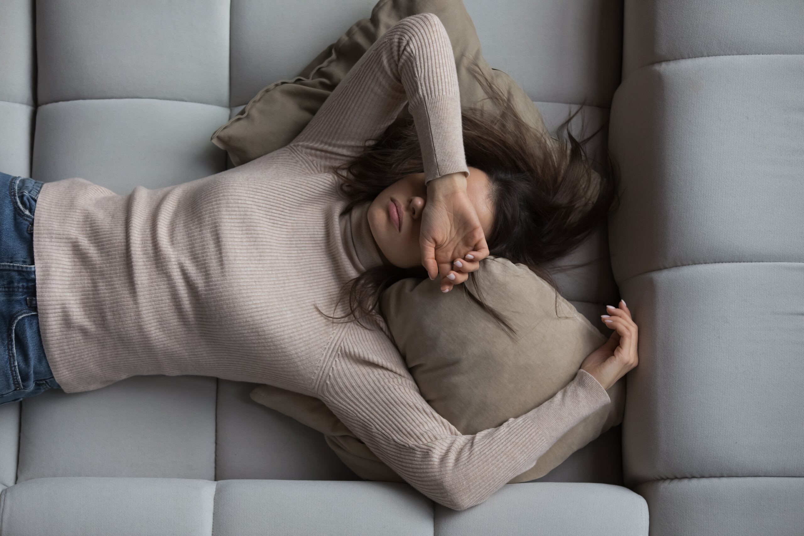 A lady lies on a sofa, with her arm resting over her eyes.