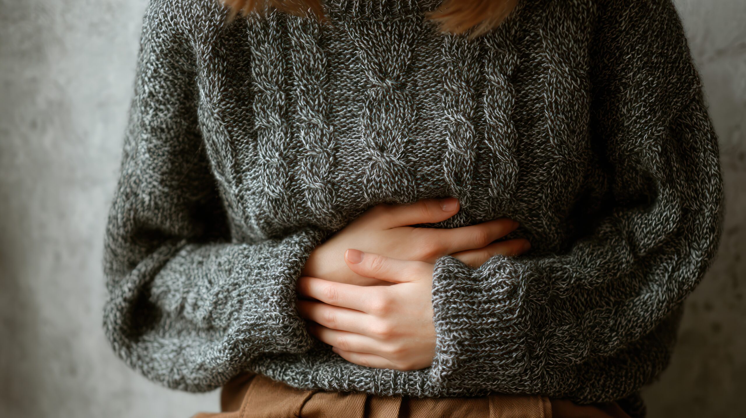 A woman in a grey sweater holds her stomach